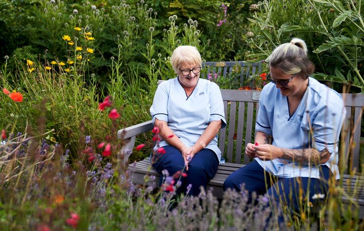 Two NHS Lothian staff laughing sitting on a bench in Belhaven Hospital Community Garden