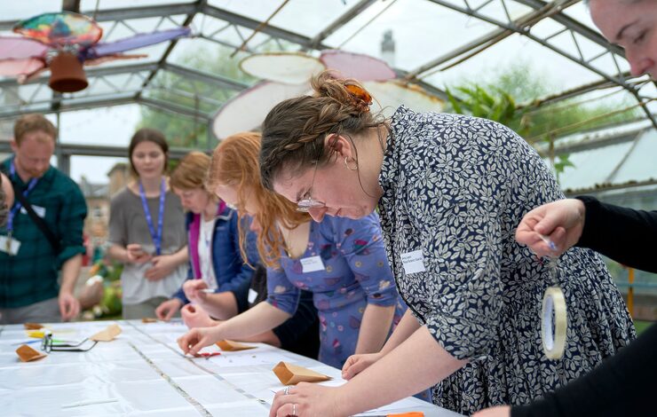 Tonic Arts Network Session in the GlassHouses at the Royal Edinburgh Hospital. People stood around a table sticking plants to a strip to create a visual diary.